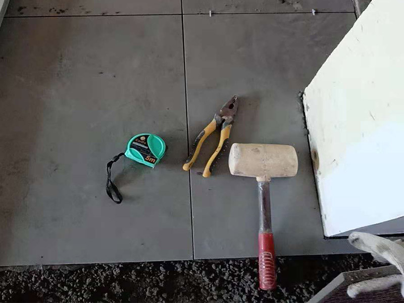 客廳地磚鋪貼：鋪貼的工具包括橡膠錘和粘結(jié)劑。在進行施工之前先把所需要的這些材料都整理好放在一旁備用；基層的處理工作對瓷磚的平整度有很大的影響，對于基層要做好清潔工作，還有找平工作。放樣：在進行瓷磚的鋪貼工作之前還事先找好垂直線，這樣可以在鋪貼的時候找到瓷磚的水平線，讓瓷磚鋪貼的更加的平整。粘結(jié)劑加水?dāng)嚢杈鶆?，靜置10分鐘之后就可以使用。將瓷磚表面的浮灰清除，再在瓷磚背面均勻的涂抹上粘結(jié)劑，按照預(yù)鋪的順序?qū)⒋纱u鋪貼在地面上，最后用橡膠錘輕輕拍打至服帖齊整。